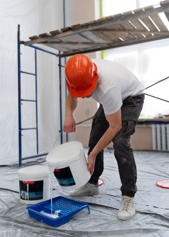 Peintre dans un chantier verse de la peinture dans le bac a peinture d'un pièce bâchée et protégée